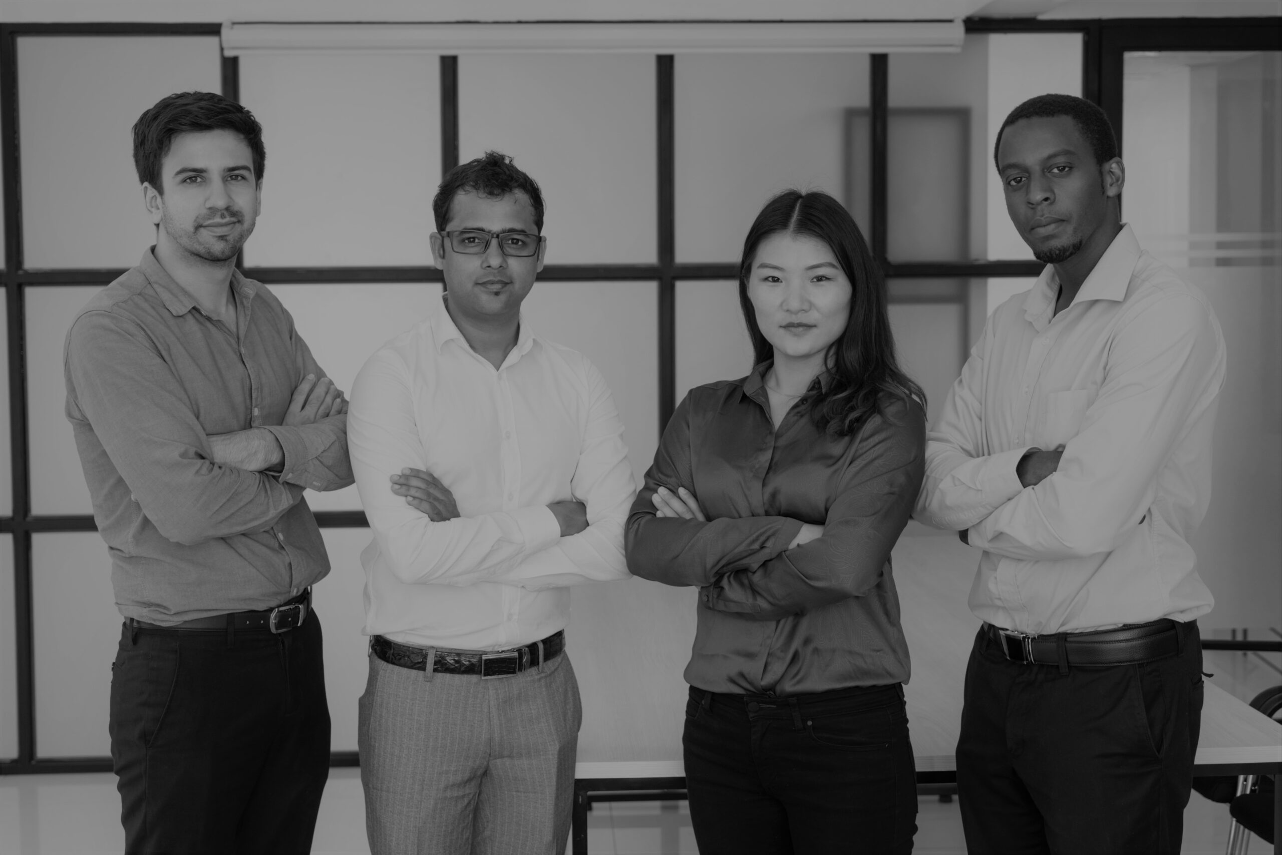 Multiethnic work group posing in modern office. Portrait of four professionals with arms crossed, glass business interior in background. Professional team concept