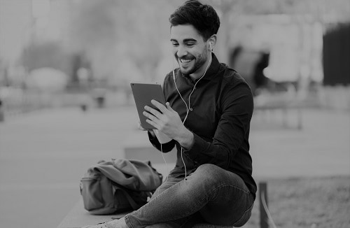 Portrait of young man having a video call on digital tablet while sitting on bench outdoors. Urban concept.