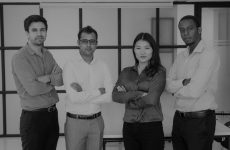 Multiethnic work group posing in modern office. Portrait of four professionals with arms crossed, glass business interior in background. Professional team concept
